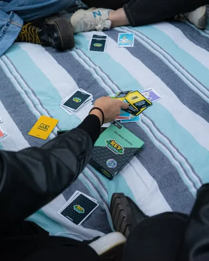 Grupo jugando a Rey Mono sentado sobre una manta de rayas, con las cartas repartidas y el mazo en el centro