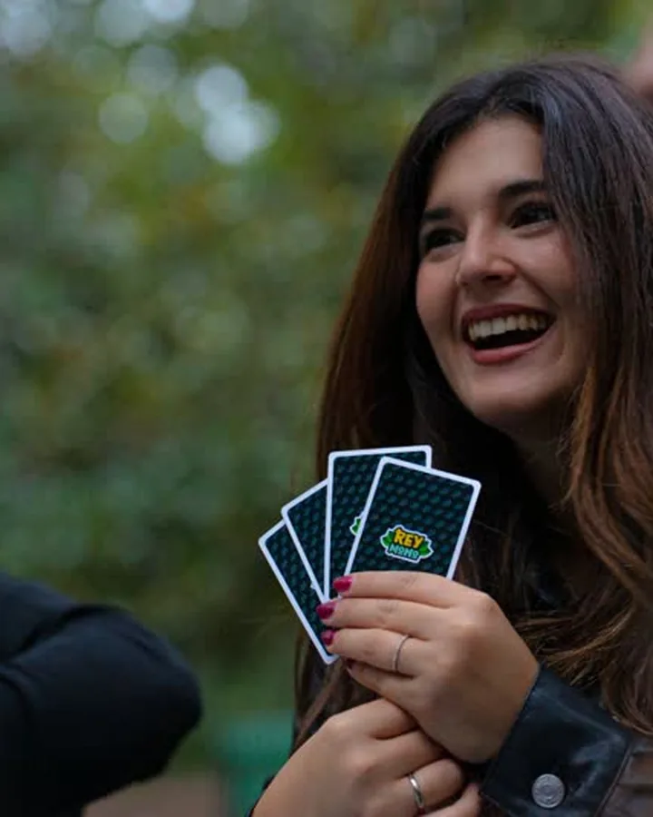 Jugadora riéndose con su mano de cartas de Rey Mono durante una partida al aire libre