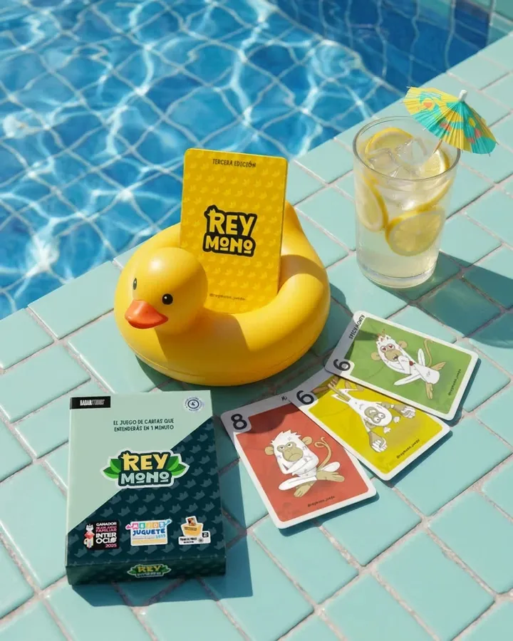 Caja de Rey Mono y cartas junto a una piscina, con un flotador de pato y una limonada
